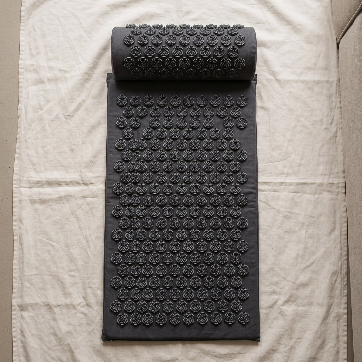 Dark gray acupressure mat and neck pillow on ivory linen