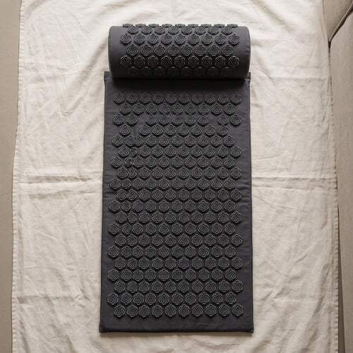 Dark gray acupressure mat and neck pillow on ivory linen